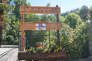 Une enseigne en bois sur laquelle est inscrit « Le Matin d’Altos », entourée de fleurs et de verdure.
