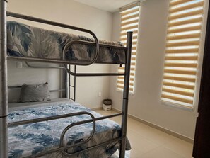 Una cama litera con ropa de cama estampada, una mesita de noche pequeña y una ventana con persianas.