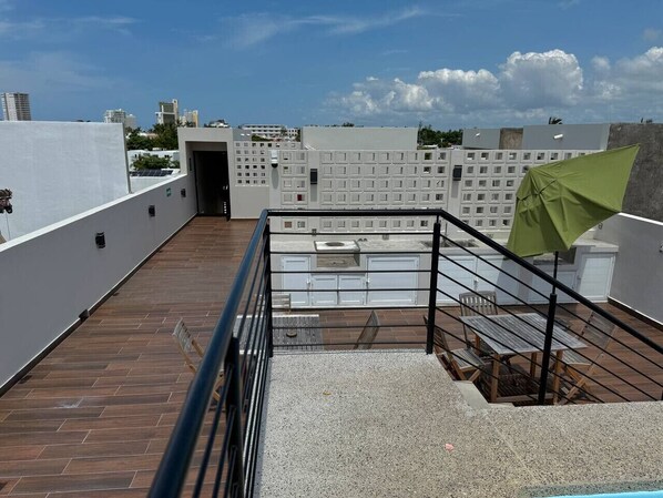 Une terrasse sur le toit, dotée d’une plateforme en bois, d’une rambarde en métal et d’un parasol vert.