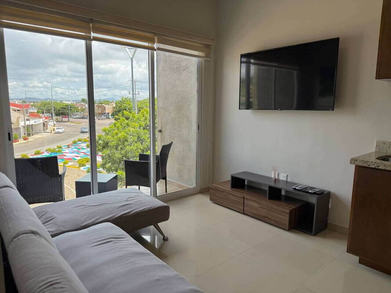 Een moderne hotelkamer met een grote schuifdeur naar een buitenruimte, een flatscreen televisie aan de muur, een bank en een klein bijzettafeltje.