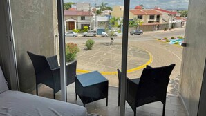 A balcony with wicker chairs and a small table, overlooking a parking area and buildings.