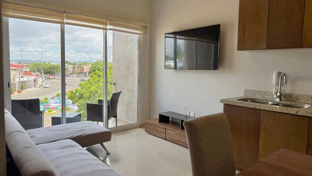 A modern apartment with a balcony, a flat-screen TV, a kitchen with a sink, and a dining area.