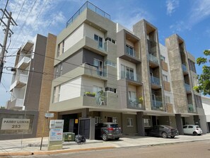 Un edificio residencial de varios pisos con balcones, un estacionamiento y un cartel con el número de la dirección.