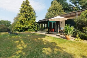 Een modern huis met een glazen patio, een gazon en een grote boom.