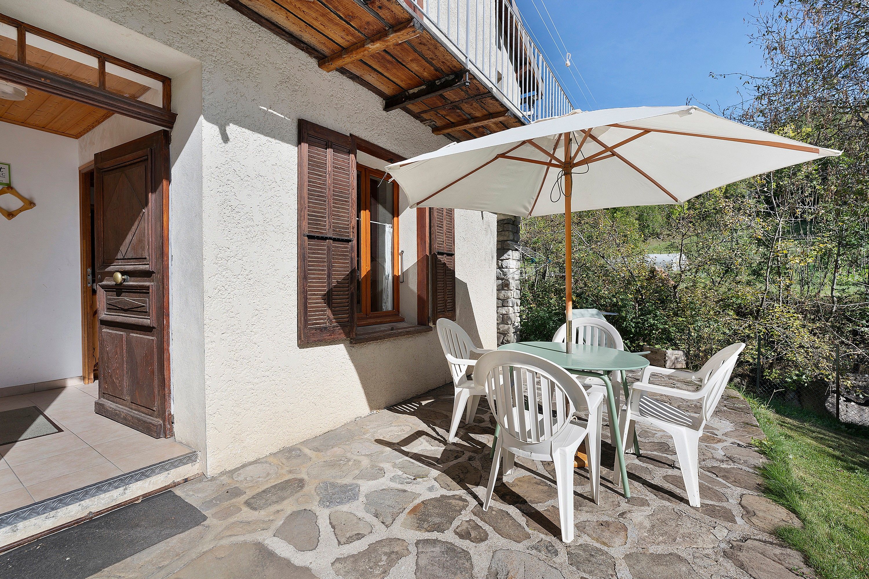 A patio with a table and chairs, a white umbrella, and a stone floor.