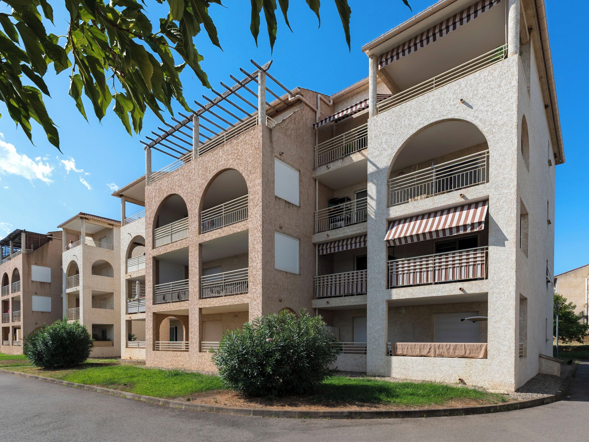 Un immeuble résidentiel à plusieurs étages, doté de balcons, de fenêtres en arc de cercle et surplombant un ciel dégagé.