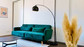 A teal sofa, a black floor lamp, a small round table, and a tall plant with pampas grass. - Juni - Air-conditioned & Balcony (Brignoles)