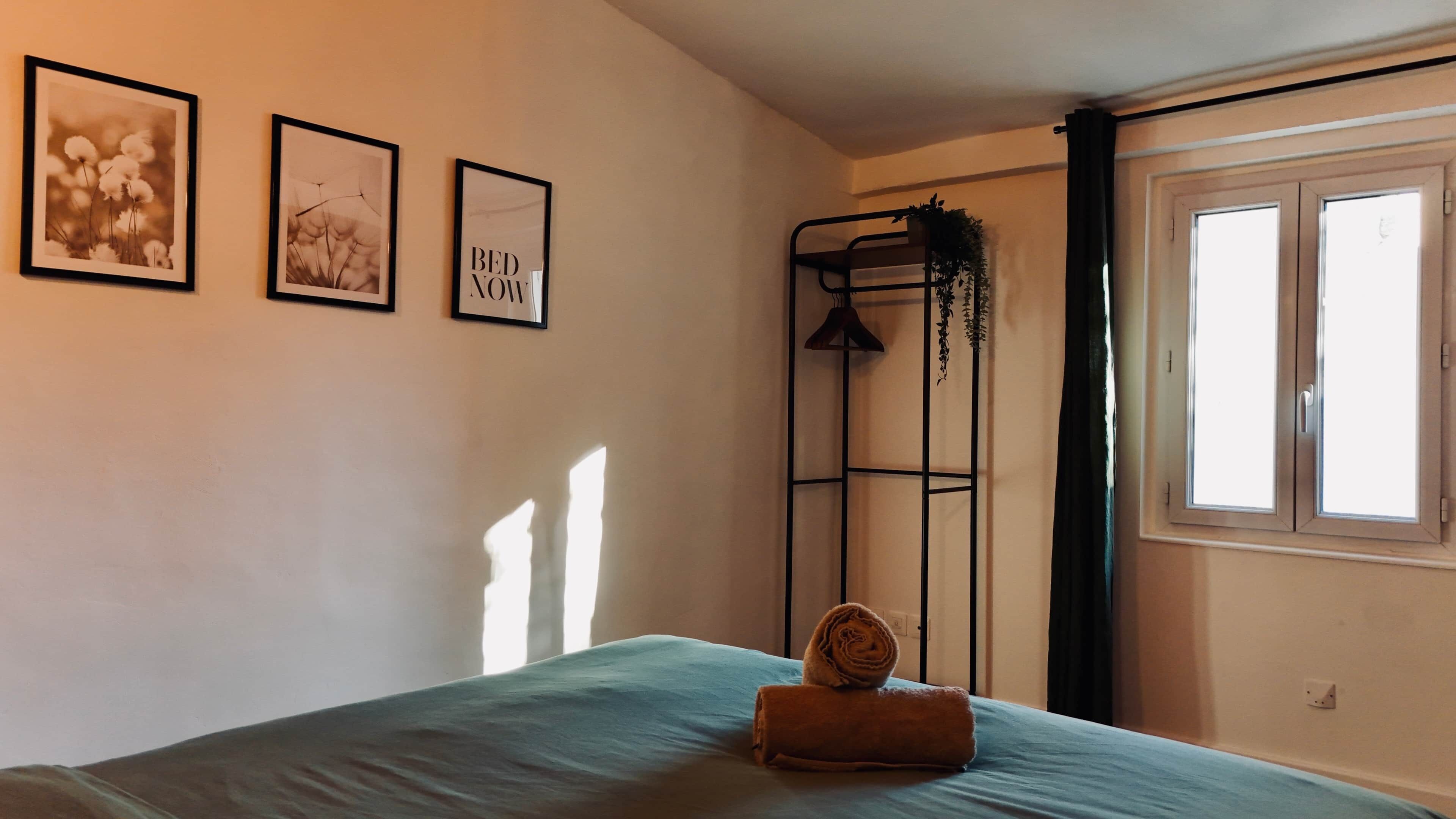 A bedroom with a bed, a window, and three framed pictures on the wall.