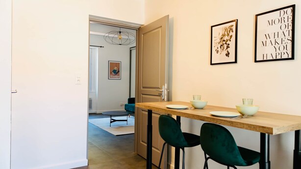 A dining area with a wooden table, two green chairs, and a few bowls and plates. - Juni - Air-conditioned & Balcony (Brignoles)