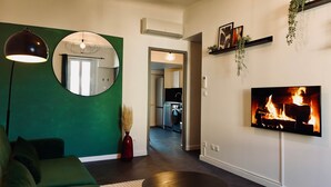 A modern living room with a green accent wall, a round mirror, a floor lamp, a fireplace, and a kitchen visible through an open door. - Juni - Air-conditioned & Balcony (Brignoles)