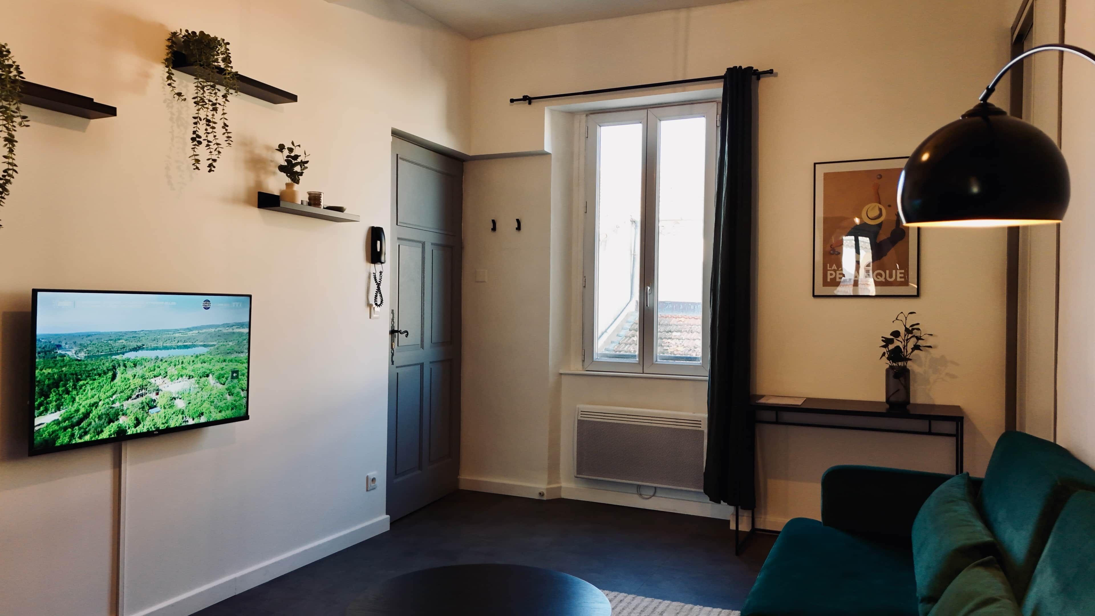 Ett vardagsrum med en tv, en svart lampa, en turkos soffa och ett fönster med gardiner.