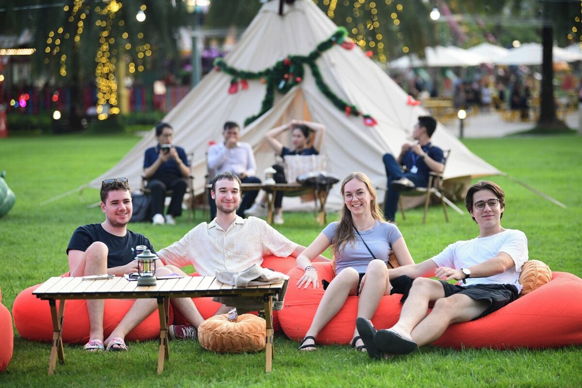 A group of people sitting on bean bags and chairs in a grassy area with a tent in the background.