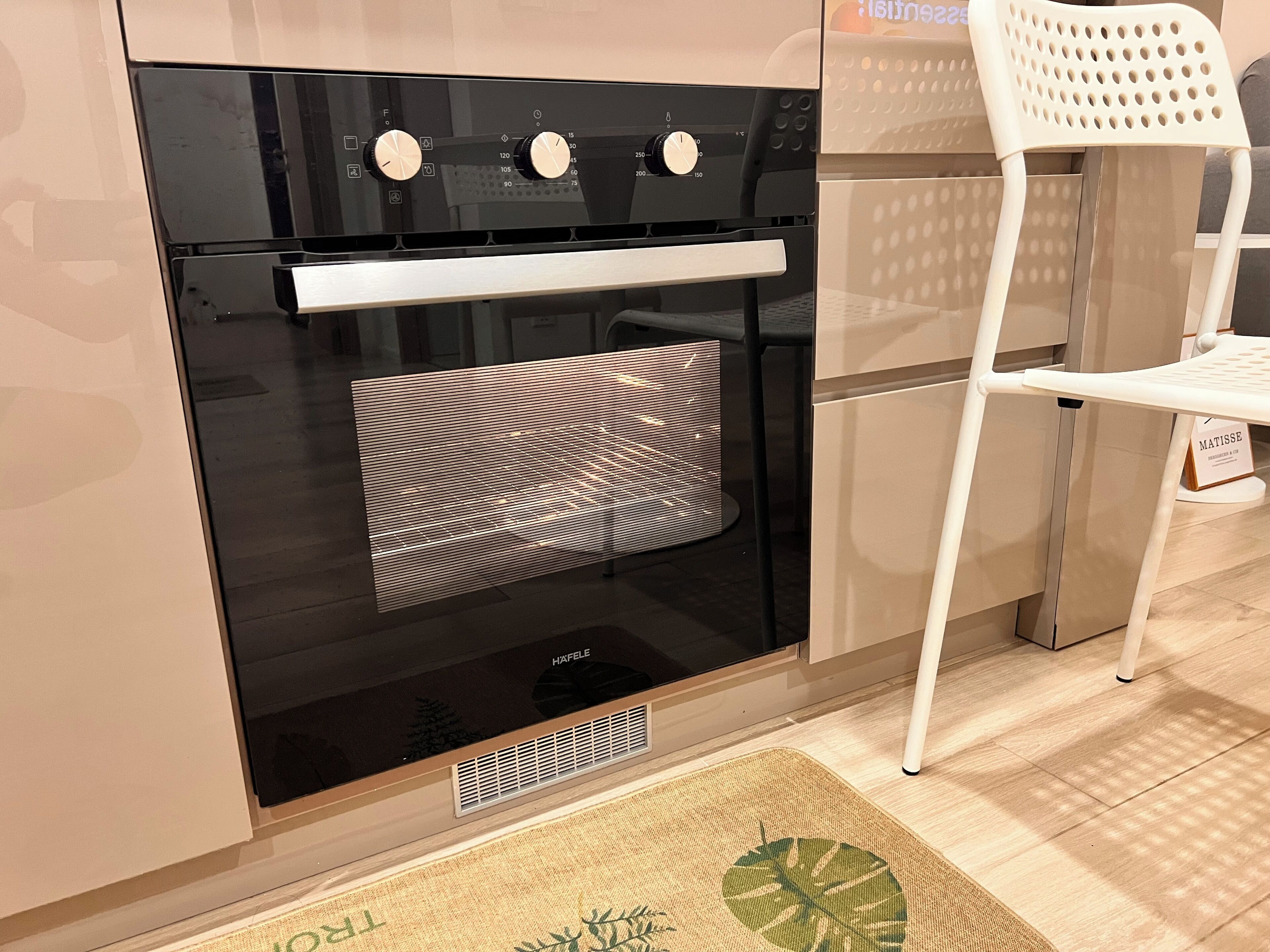 Una cocina con un horno negro, una silla blanca y un tapete con un diseño de hojas en el suelo.