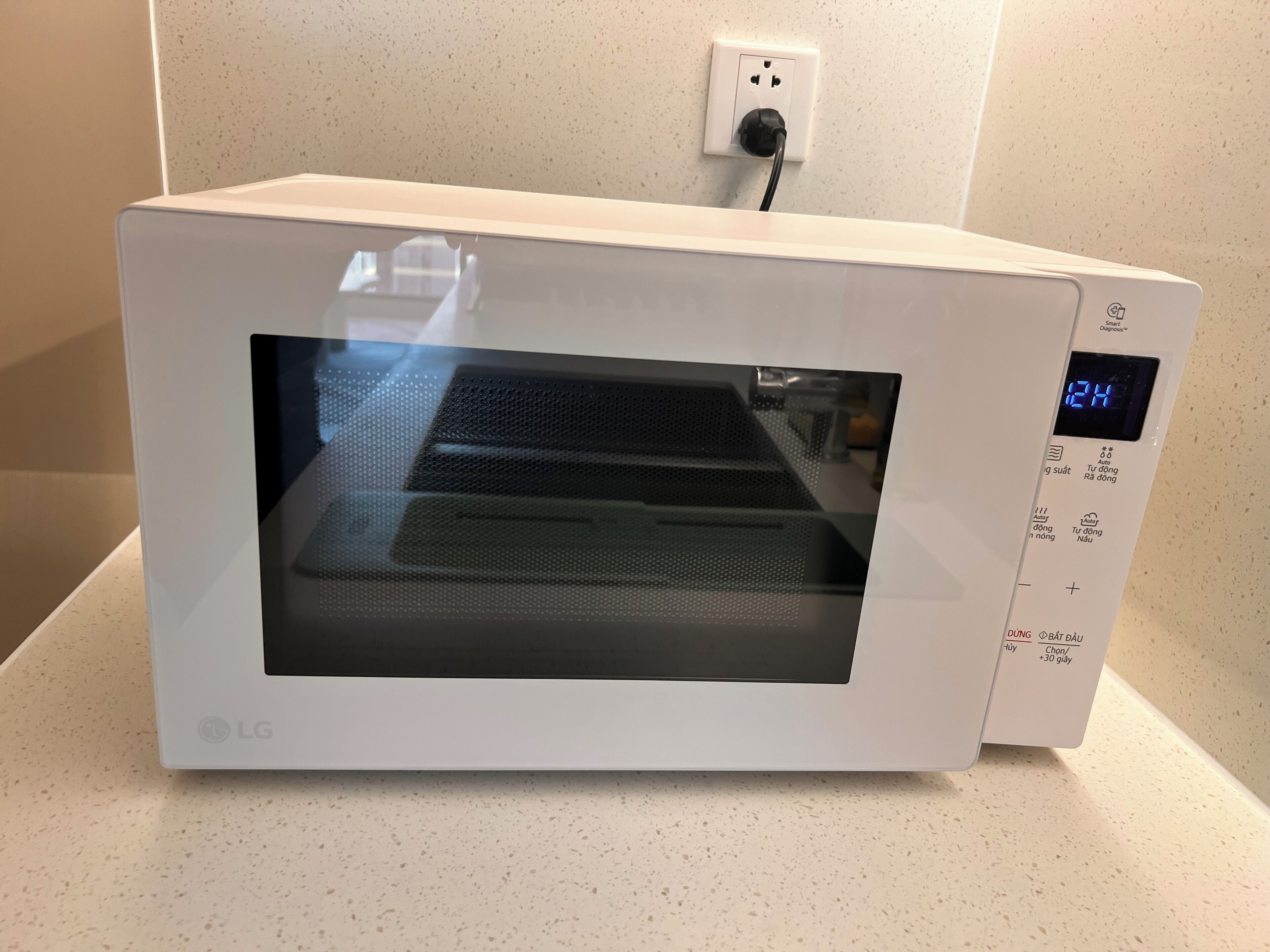 A white LG microwave oven with a digital display, placed on a speckled countertop.