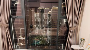 A bedroom with a large window, a bed with floral bedding, and a view of a cityscape with illuminated buildings. - Vinhomes Grand Park-Masterise Center (Ho Chi Minh City)