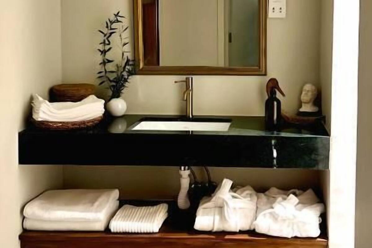Un baño con un espejo grande, un lavamanos y repisas con toallas.
