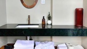 Een badkamer met een ronde spiegel, een wastafel en een badkamermeubel met handdoeken en toiletartikelen.