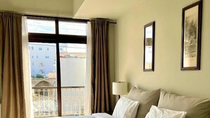Een hotelkamer met een groot bed, een balkon met gordijnen en twee ingelijste foto’s aan de wand.