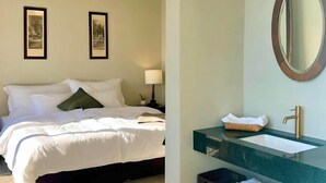 Hotelkamer met een bed, twee ingelijste foto's aan de muur, een bedlampje, een spiegel en een wastafel met handdoekhouder.