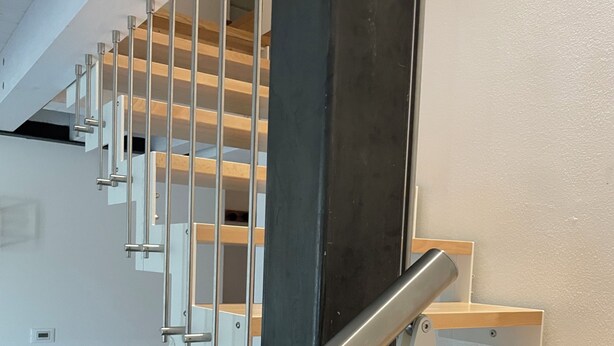 Een moderne trap met metalen leuningen en houten treden, die naar een verdieping leidt.
