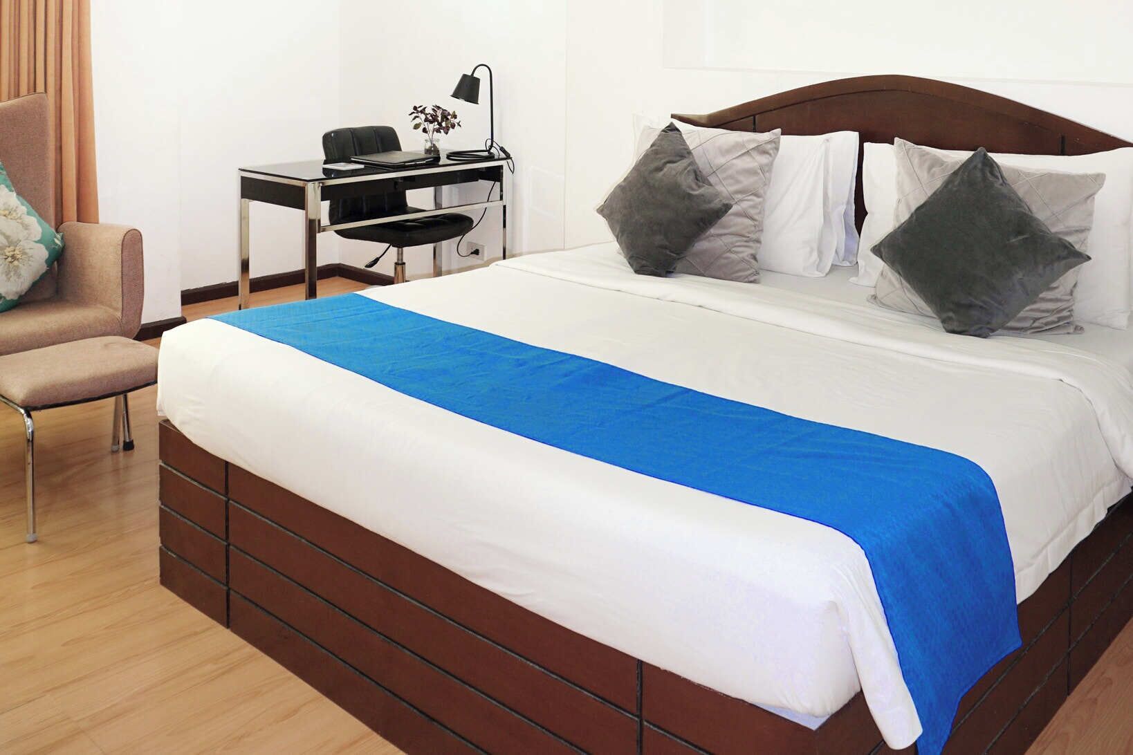 A hotel room with a large bed, a desk with a chair, and a lamp.