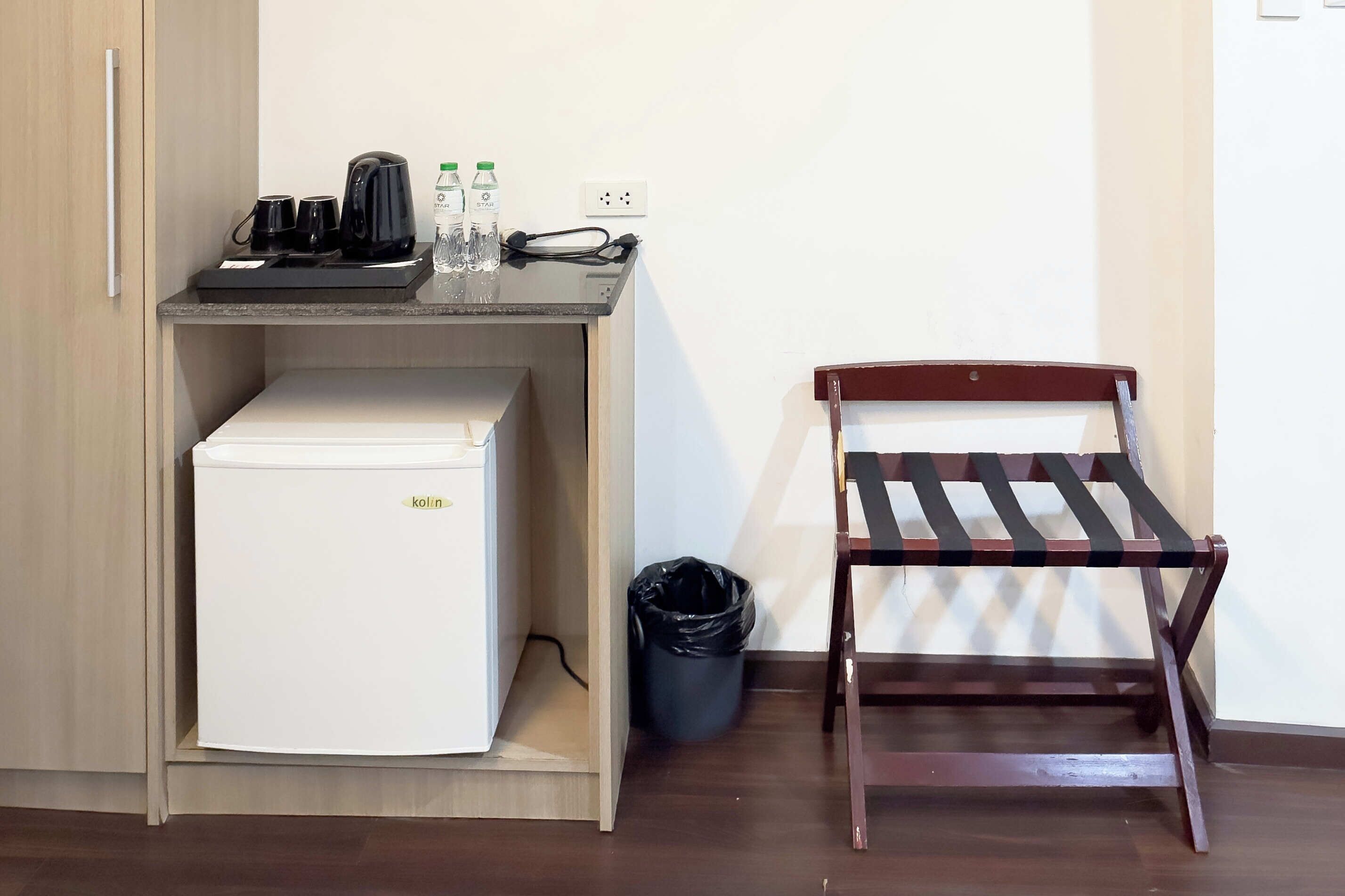 A compact kitchenette with a refrigerator, coffee maker, and water bottles. A wooden chair is positioned next to the counter.