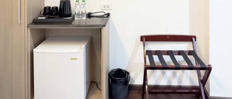 A compact kitchenette with a refrigerator, coffee maker, and water bottles. A wooden chair is positioned next to the counter.