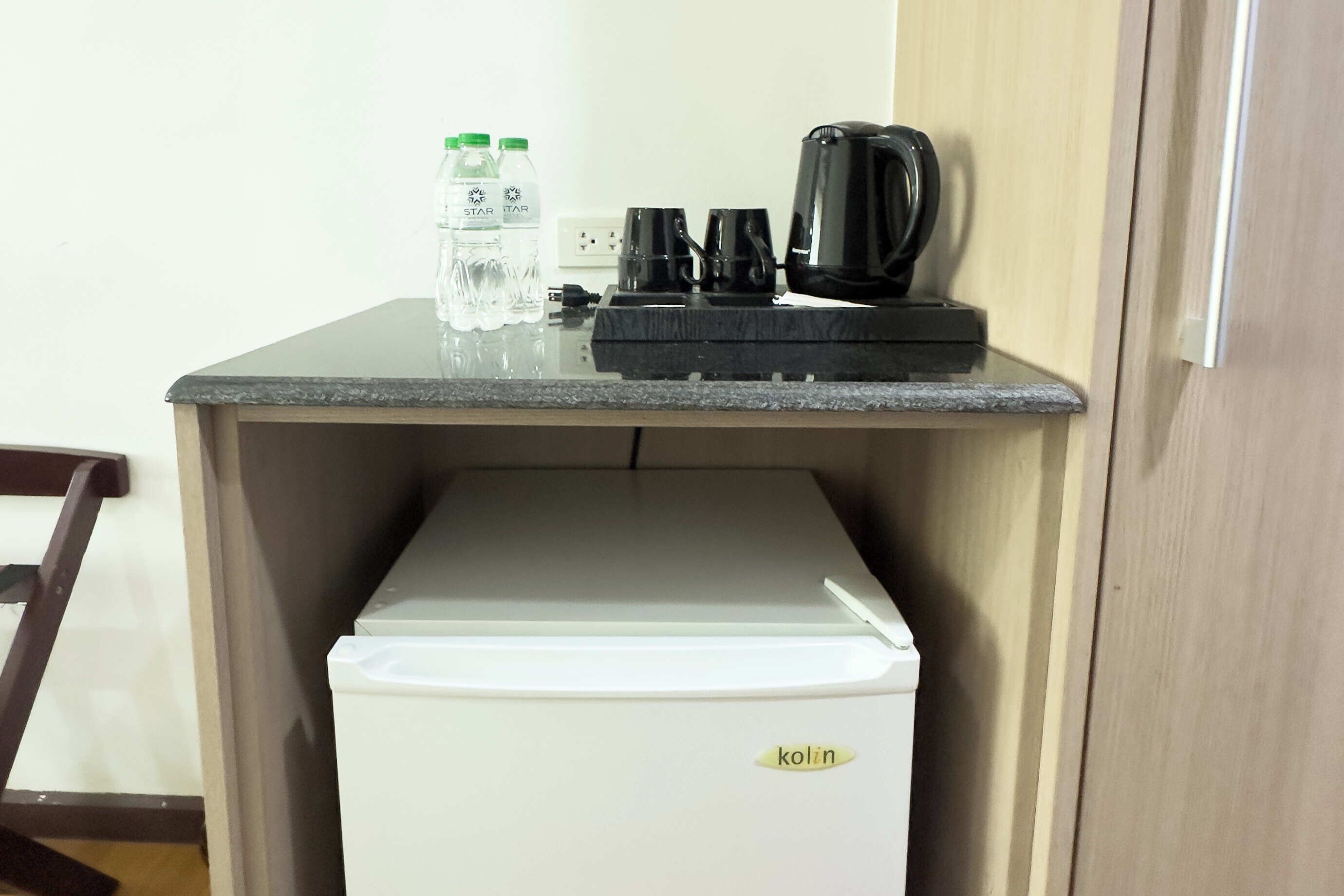 Una kitchenette con un refrigerador blanco, una cafetera y dos botellas de agua sobre una encimera.