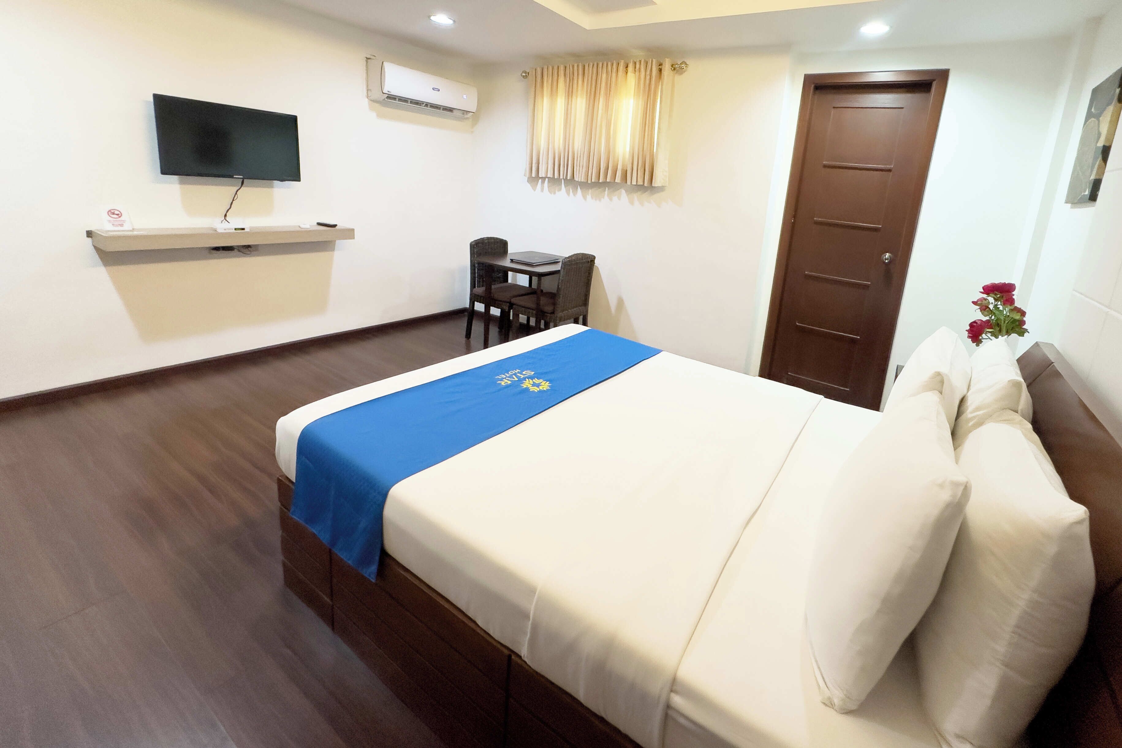 A hotel room with a bed, a TV mounted on the wall, a desk with a chair, and a door.