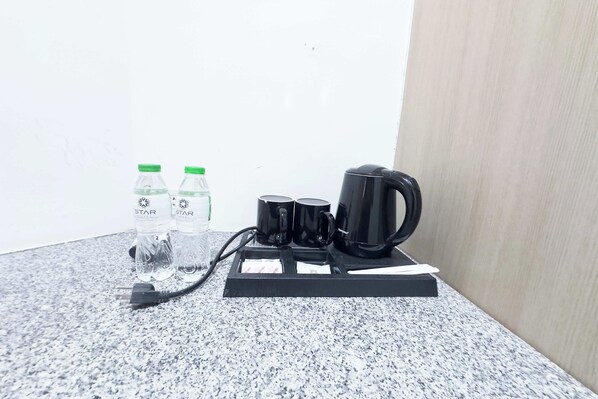 A coffee maker, two water bottles, and two black mugs on a granite countertop.