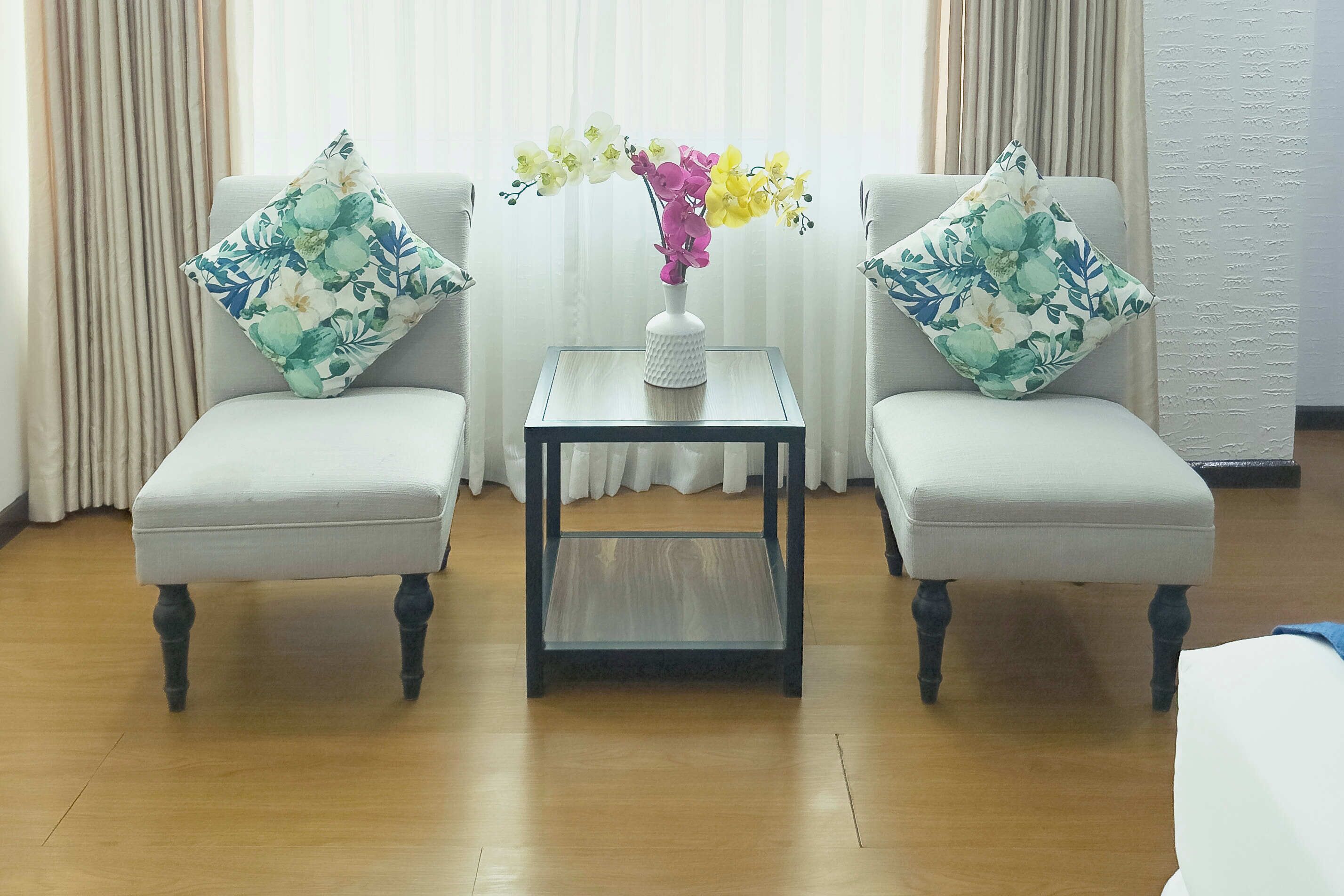 A room with two armchairs, a small table with a vase of flowers, and a curtain backdrop.