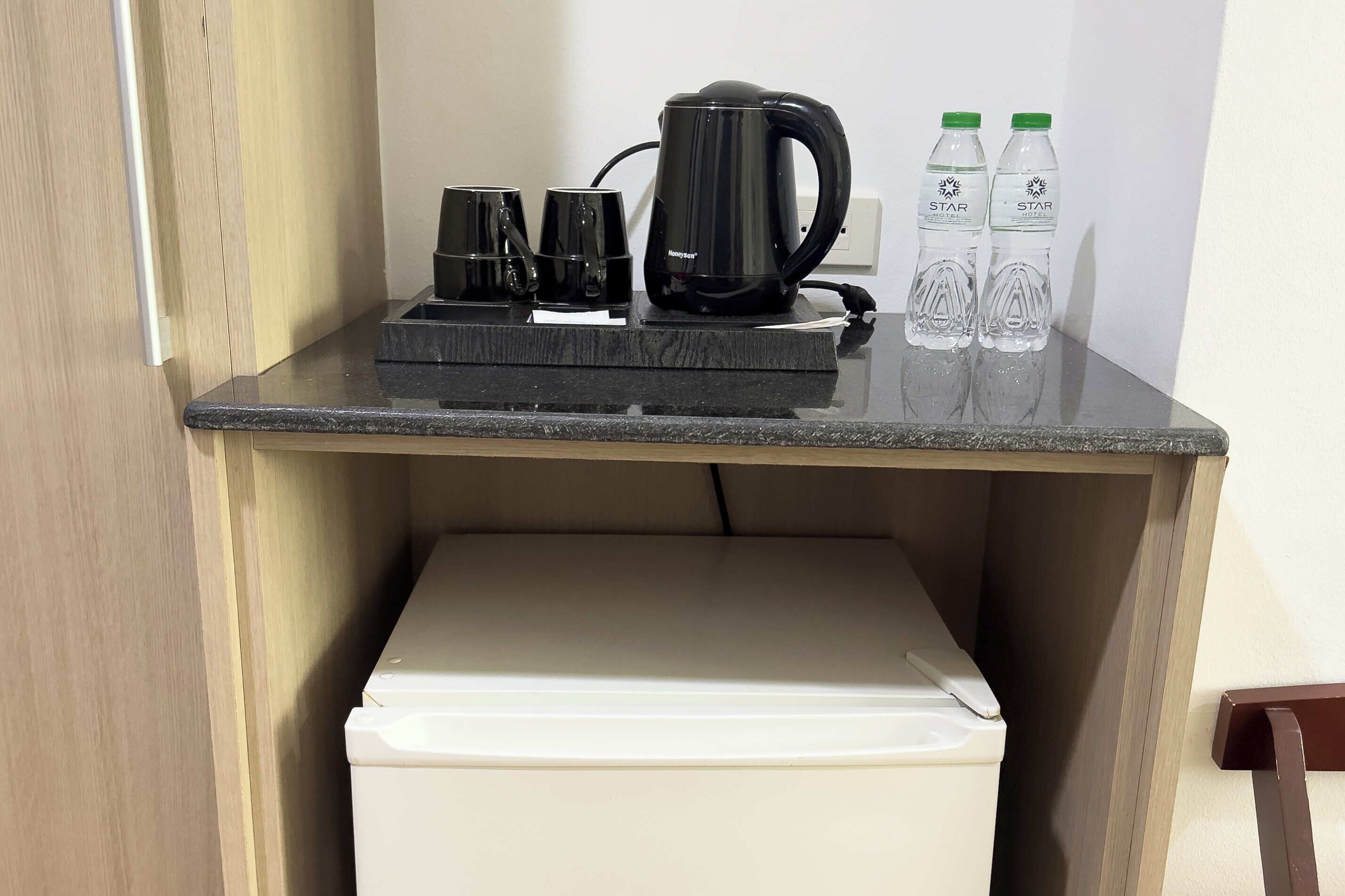 Une petite kitchenette équipée d’une machine à café, de deux tasses et de deux bouteilles d’eau, le tout posé sur un plan de travail.