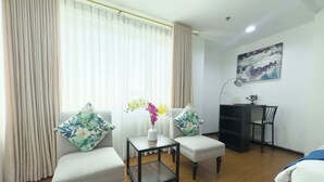 A living room with two white armchairs, a small table with a vase of flowers, and a desk with a chair. - Star Hotel Davao (Davao)
