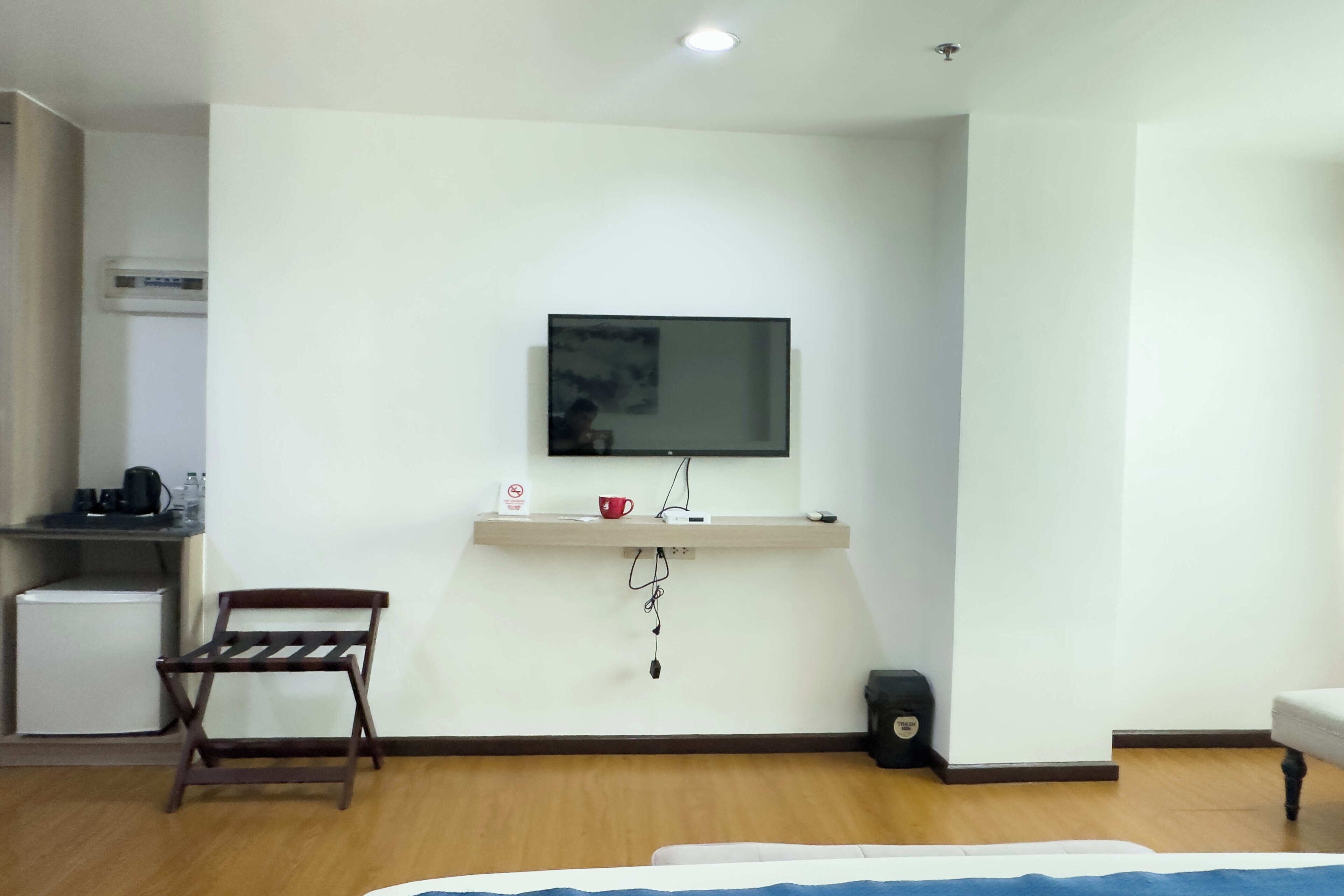 Une chambre d’hôtel comprenant un lit, un petit bureau avec une chaise, un téléviseur fixé au mur, une machine à café et une poubelle.
