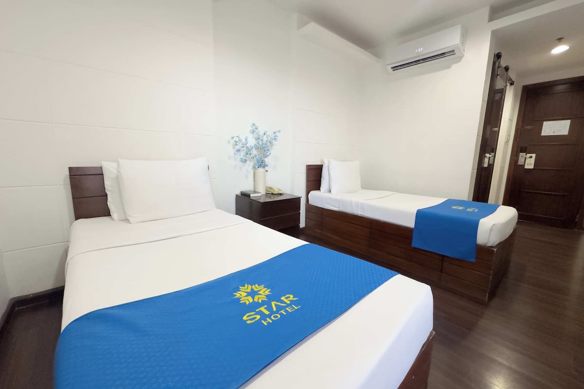 A hotel room with two beds, a nightstand, a vase with flowers, and a wooden door.