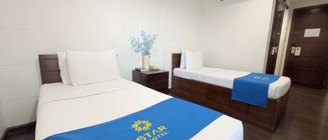 A hotel room with two beds, a nightstand, a vase with flowers, and a wooden door.