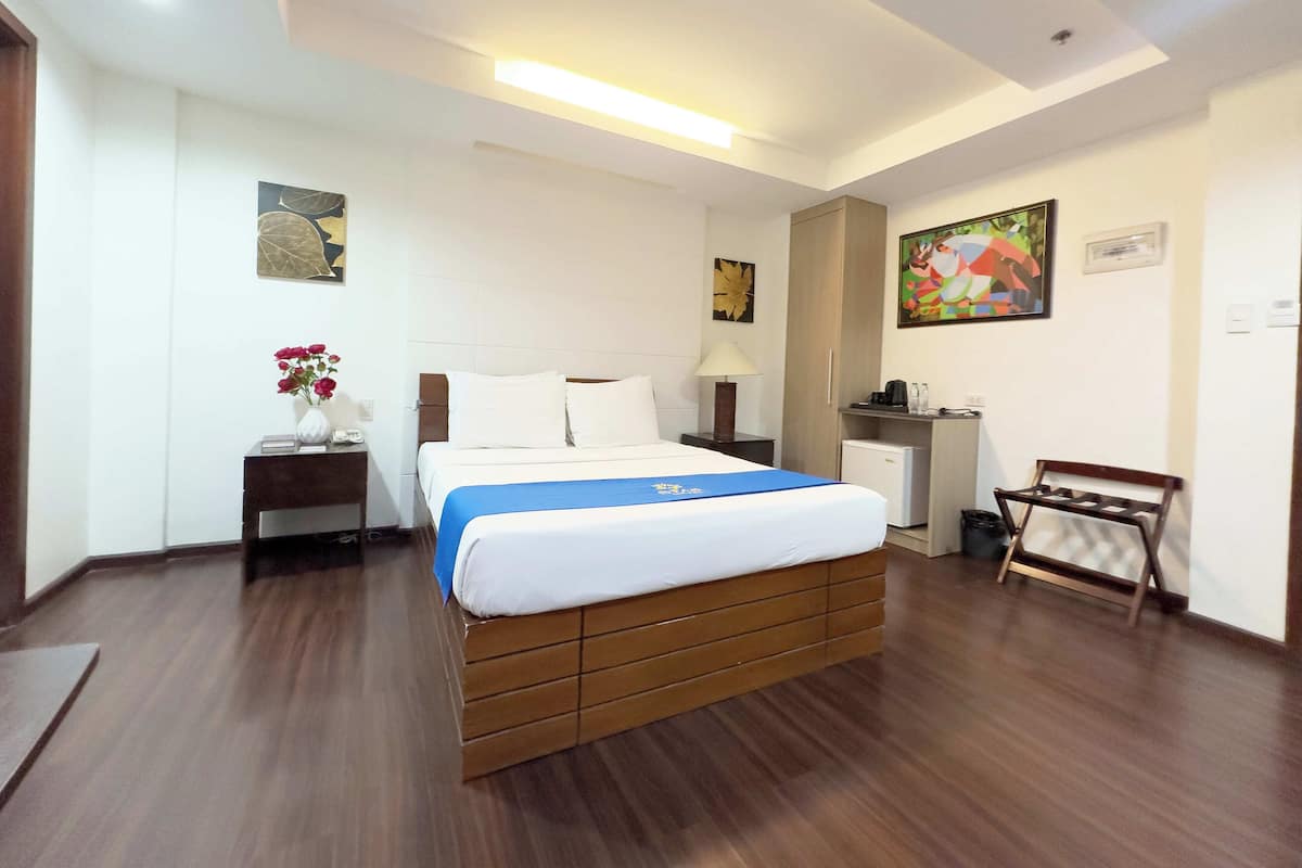 A hotel room with a wooden bed, a nightstand, a desk, and a chair.
