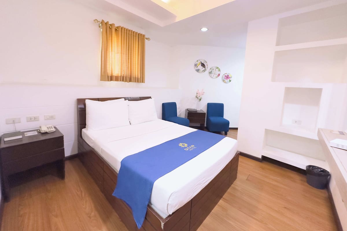 A hotel room with a bed, bedside table, and a small desk with a chair.