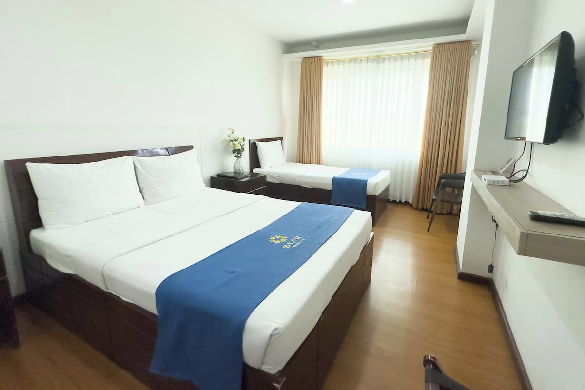 A hotel room with two beds, a TV, a desk, and a window with curtains.