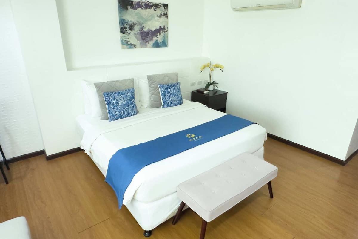 A neatly made bed with a blue bedspread and a bench at the foot of the bed.