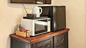 A kitchenette with a microwave, kettle, and coffee maker on a wooden cabinet.