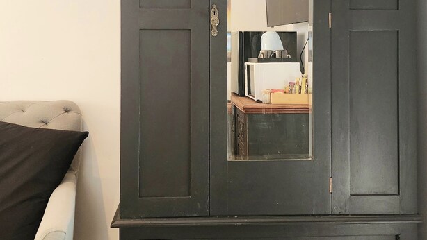 A dark wooden wardrobe with a mirror, two drawers, and decorative handles.