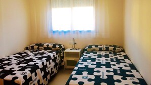 Ein kleines Zimmer mit zwei Betten, jedes mit einer deckenartigen Auflage mit Puzzle-Muster und einem kleinen Nachttisch mit einer Lampe.