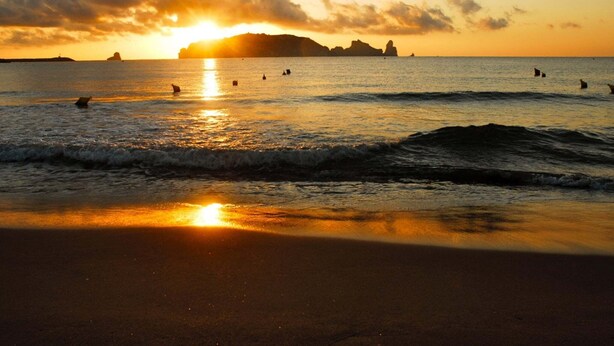A beach at sunset with waves and silhouettes of people in the water. - Els Pins apartment in Estartit (Estartit)