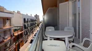 A balcony with a table and chairs, a view of the street below, and a building with balconies. - Els Pins apartment in Estartit (Estartit)