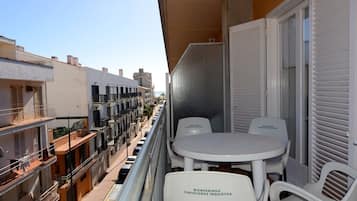 Un balcón con mesa y sillas, vista a la calle y un edificio con balcones.