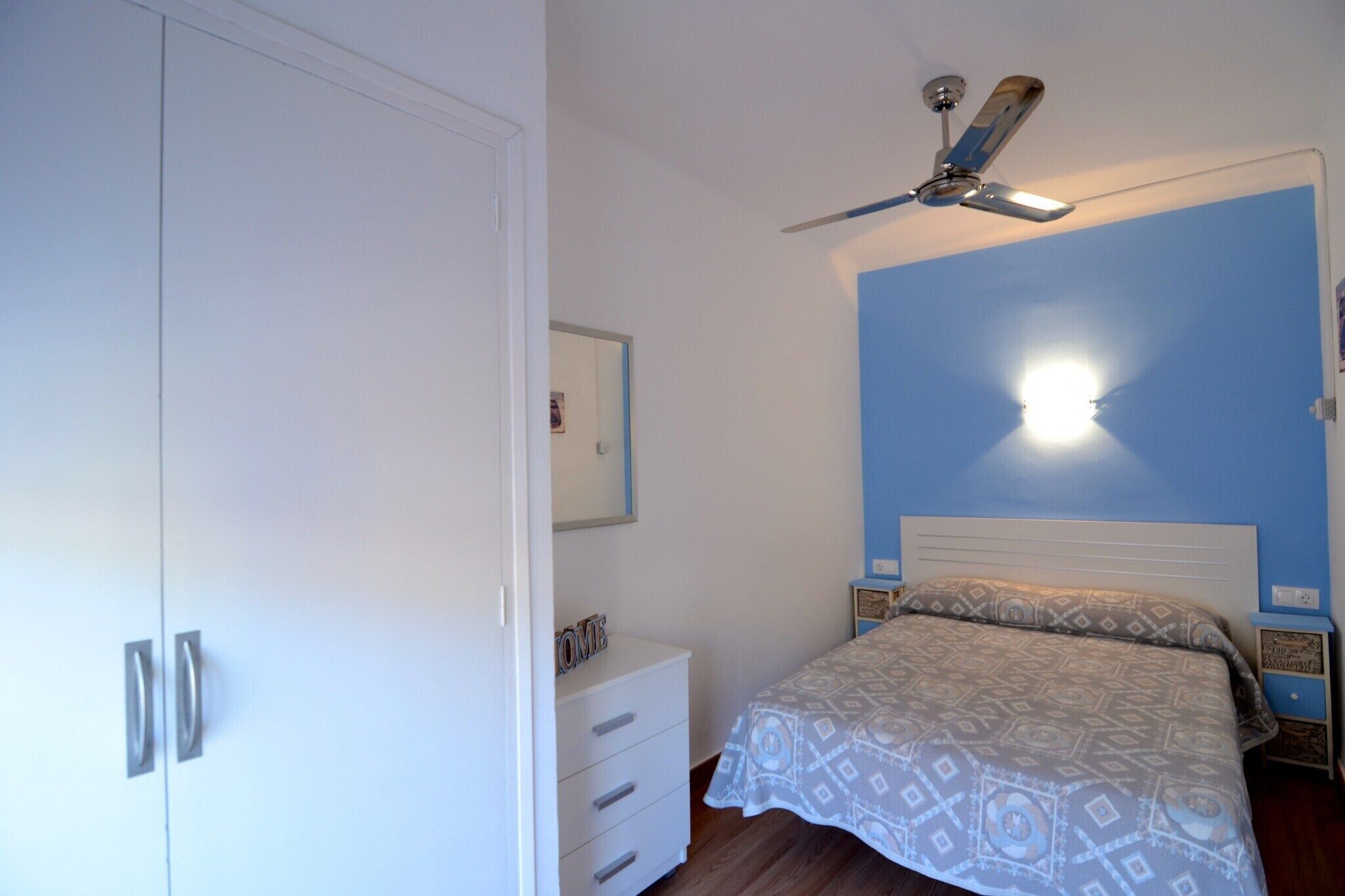 Une chambre à coucher comprenant un lit, une table de chevet, une armoire et un ventilateur de plafond.