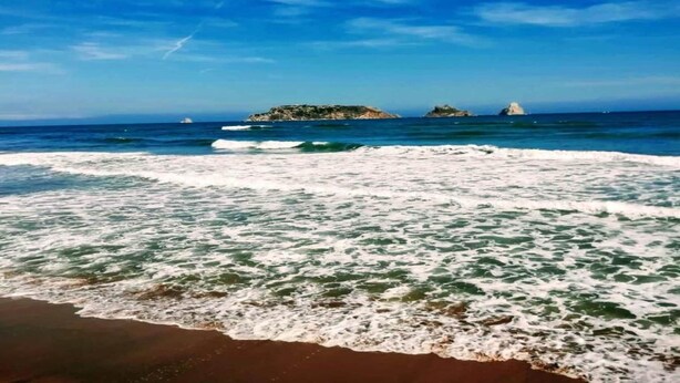 A beach with waves, a clear sky, and distant islands.
