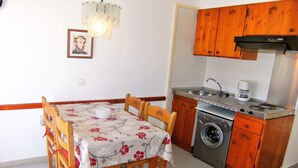 A compact kitchen with wooden cabinets, a washing machine, and a dining table with chairs.