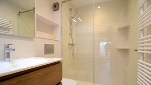 Ein modernes Badezimmer mit einer gläsernen Duschkabine, einem weißen Waschbecken und einem Holz-Waschtisch.
